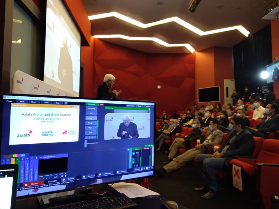vMix livefeed screen beside an investment signing ceremony in a corporate hall